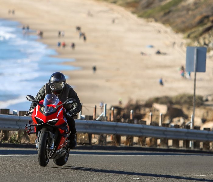 Rider on a 2021 Ducati Superleggera V4 motorcycle, riding up a hill on Pacific Coast Highway with California beach in the background