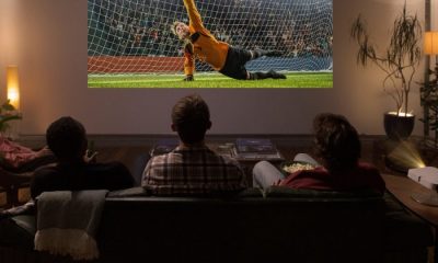 Three men sitting on couch watching soccer game off projector
