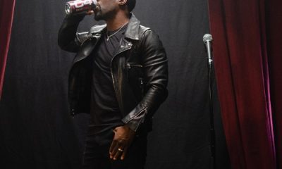 Kevin Hart in a black leather jacket stands next to a mic while drinking a can of C4 energy beverage