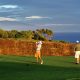 Two golfers, one taking a swing, at a golf course tee box overlooking a cliff. Golfing in Hawaii