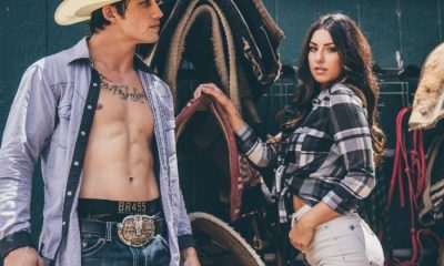 Bonner Bolton stand in the saddle room in cowboy hat and open shirt. Girl stands beside him.
