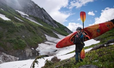 Kayaker carrying orange kayak and paddle with glacier in background