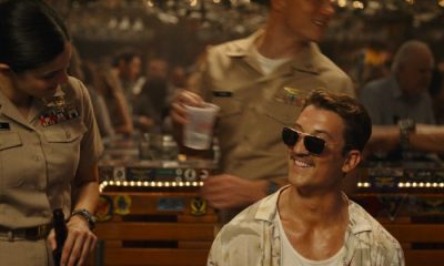 Miles Teller in shades sits at the piano during a scene from Top Gun: Maverick