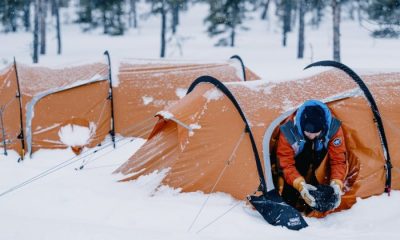 Woman holding gear as she crawls out of orange tent outdoors in snow