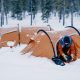 Woman holding gear as she crawls out of orange tent outdoors in snow
