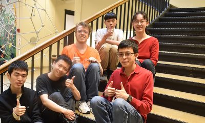 Six students sit on stairway and give the thumbs up
